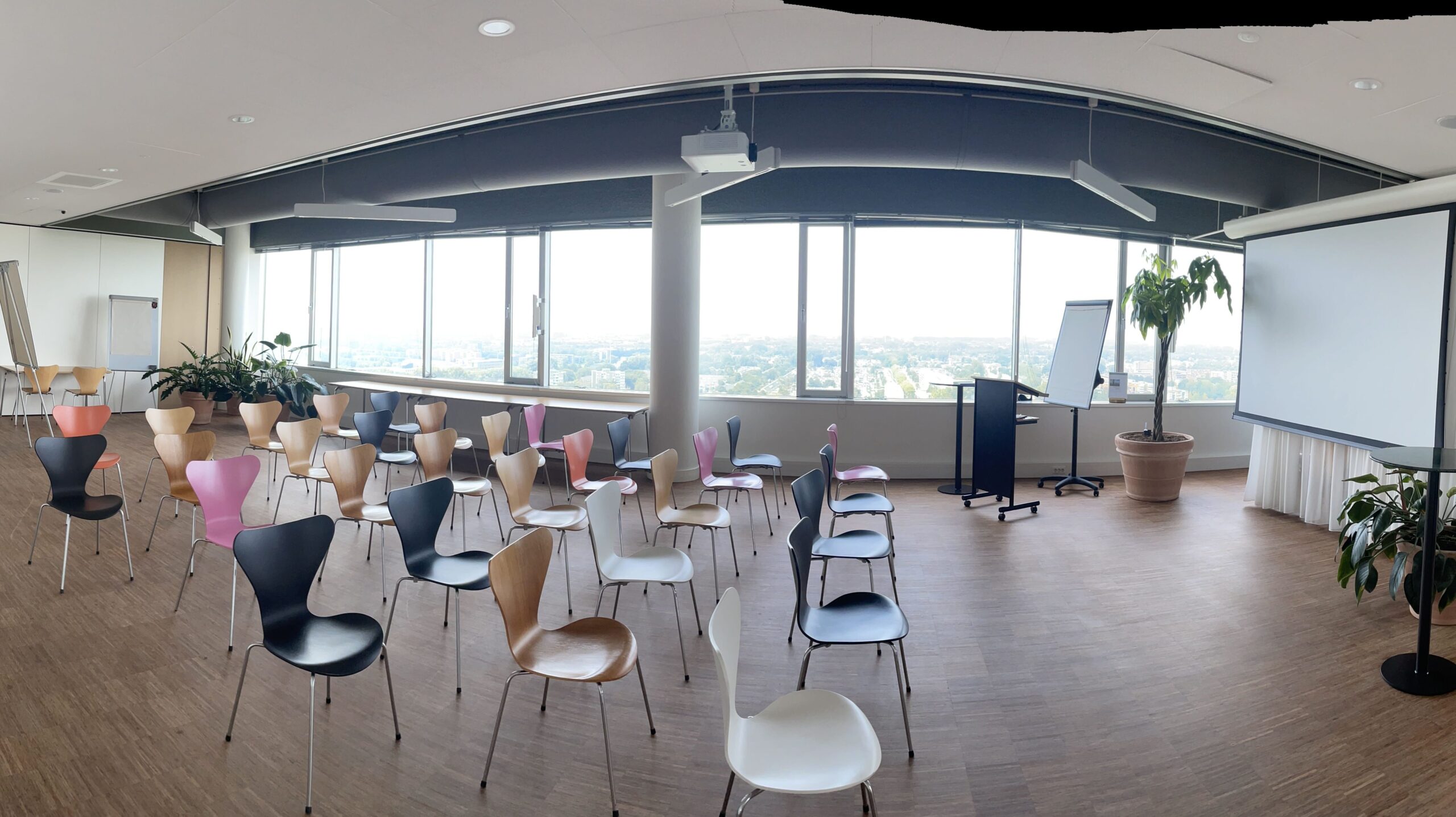 Photo of rectangular light room with multi-coloured chairs and projector and screen