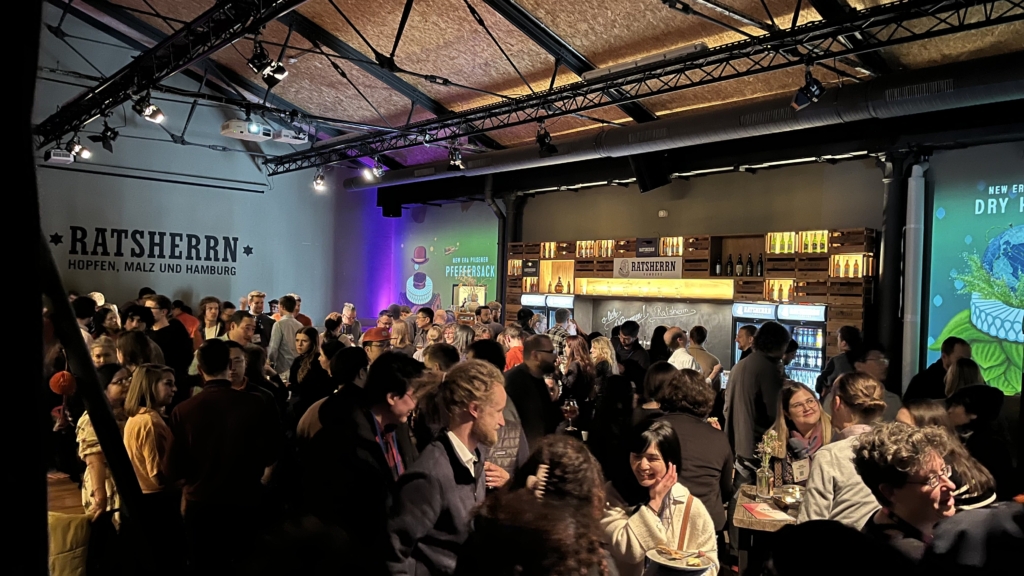 An image showing the atmosphere at the CHI NL social event in Hamburg, where several people are chatting and having drinks